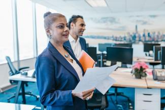 Woman in a suit holding a piece of paper. She is in an office setting.